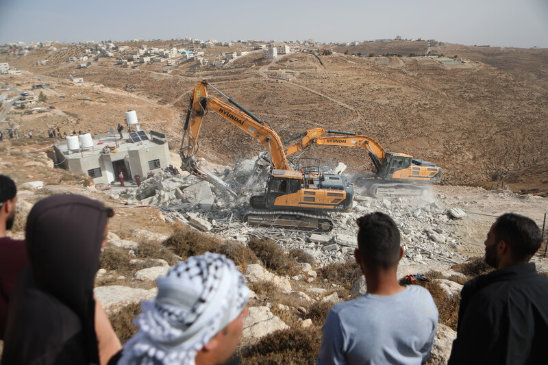 People watch two bulldozers destroy a house