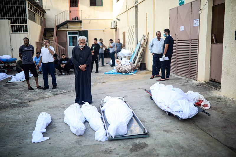 Men standing near shrouded bodies outside Al-Aqsa Martyrs Hospital in Deir al-Balah