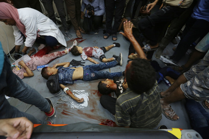 Four bloodied children lie on the ground as a medic provides treatment