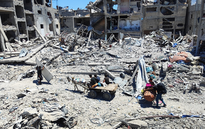 Young men push a bicycle and ride a donkey-drawn cart carrying their possessions along a bombed-out road
