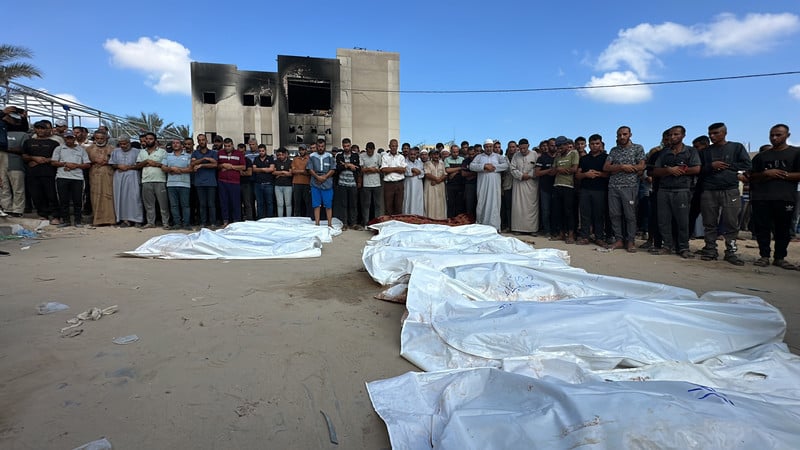 People pray over a row of shrouded corpses