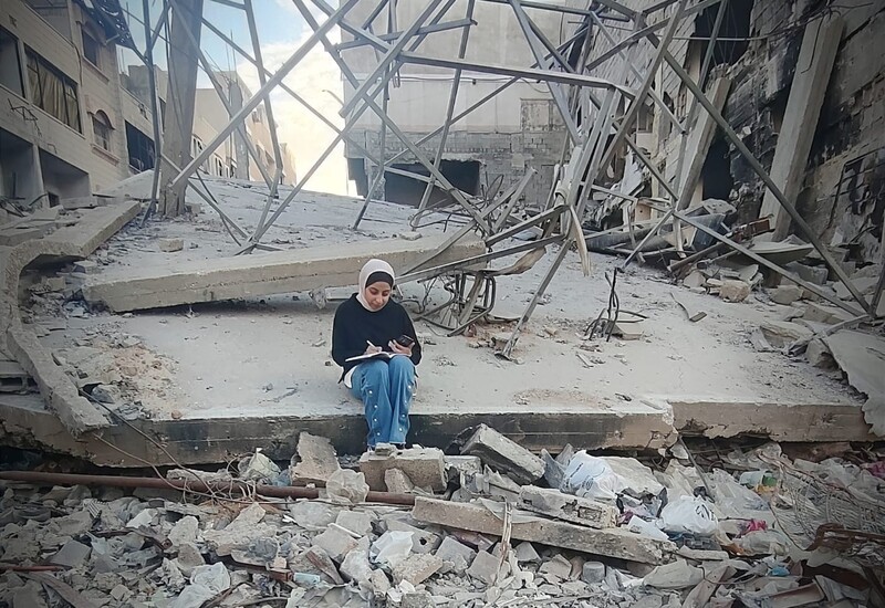 A woman sits studying in rubble