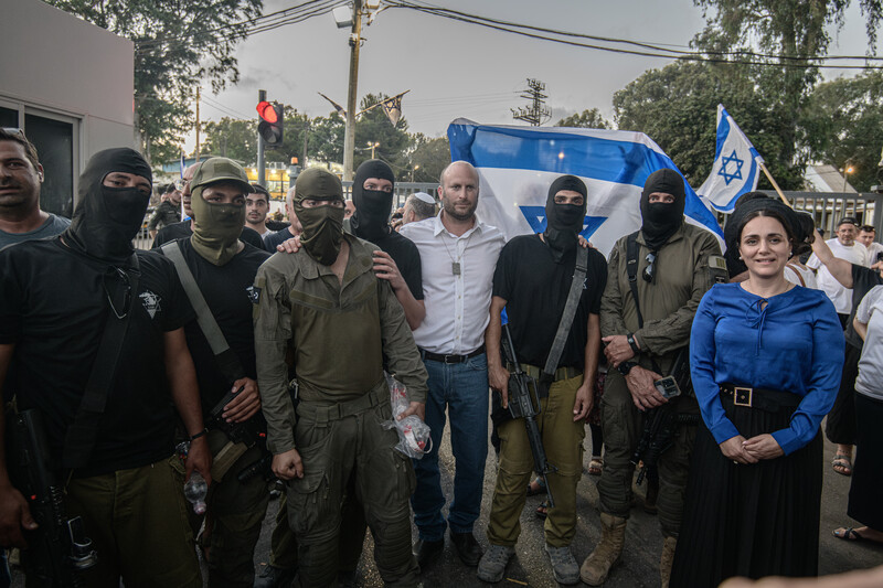 A group of masked and armed people pose with two Israeli legislators