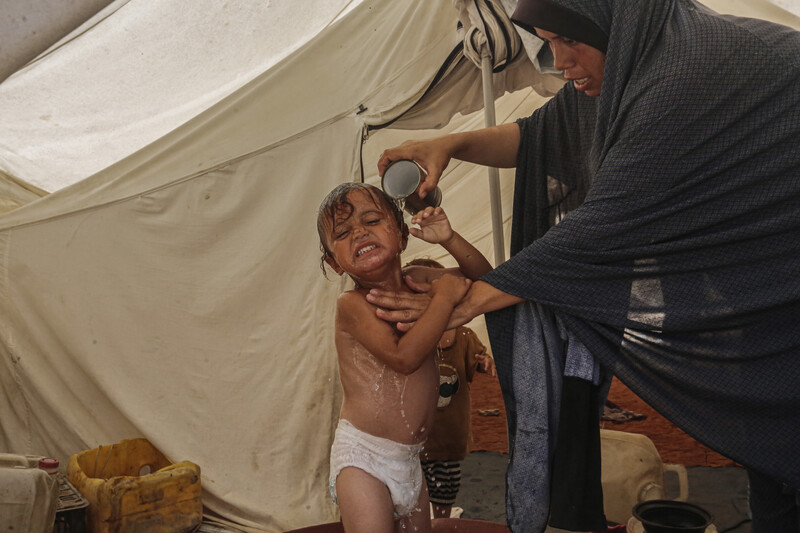 A woman bathes her child with a cup of water