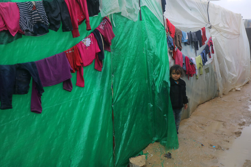 A young girl stands next to plastic sheeted tents with clothes hanging on lines