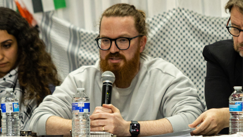 A man holds up and speaks into a microphone sitting between two people