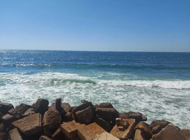 A daytime view of the blue ocean, with rocks in the foreground.