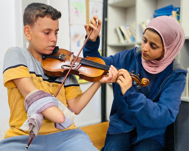 A one-handed boy practices violin with his teacher