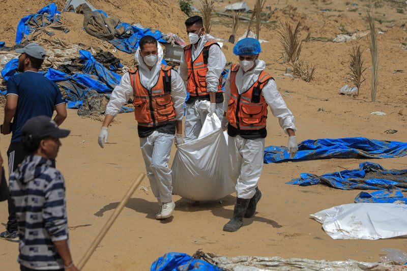 Three men in hazmat suits and face masks carry a wrapped body between them