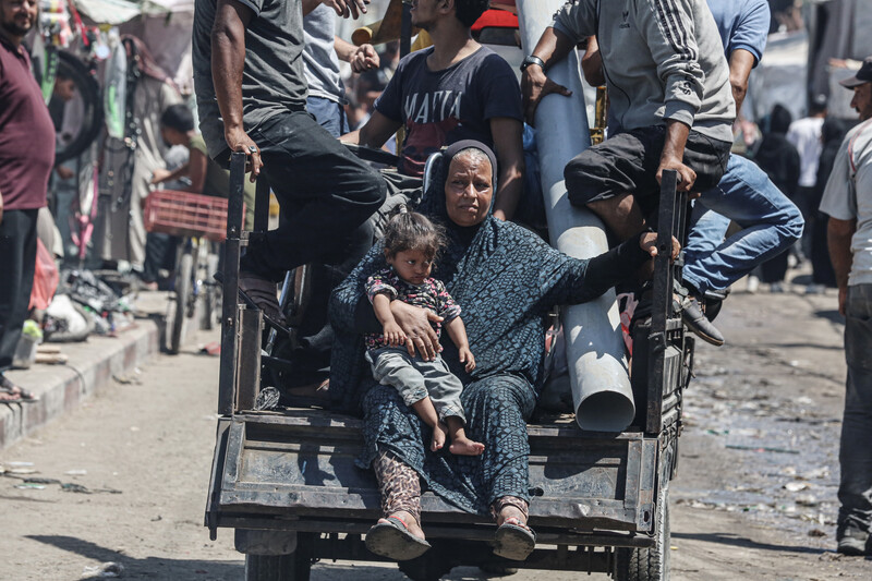 A woman and a child sit on the back of a cart pulled by a donkey