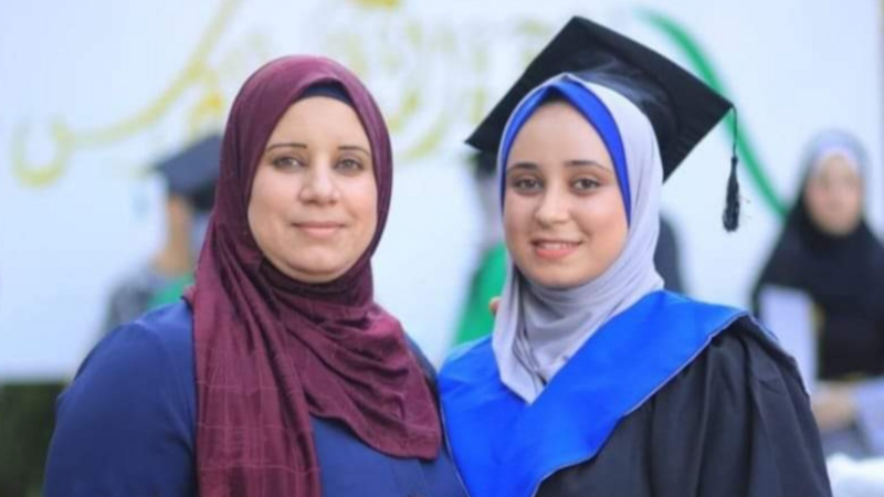 Two women, one in a graduation cap, smile for the camera.