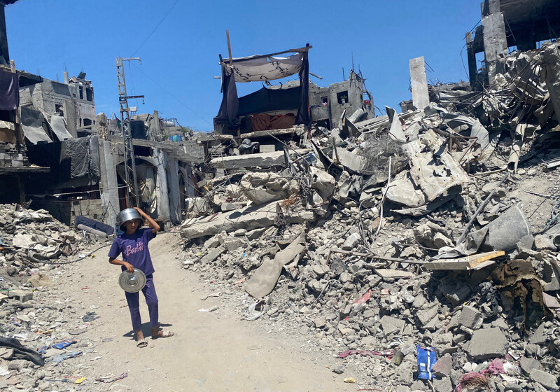 A boy wearing a pot as a helmet walks through rubble