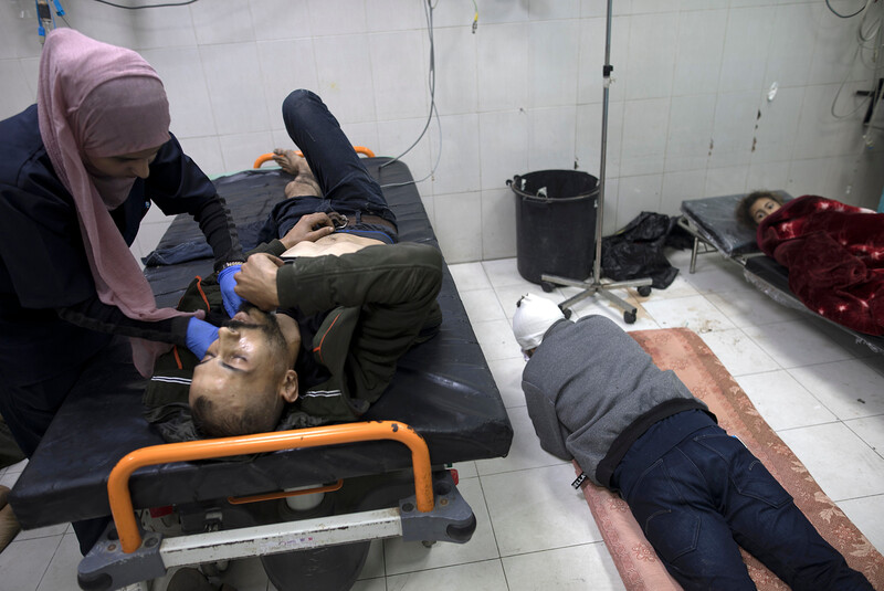 Two patients lie on the floor next to one occupied hospital bed