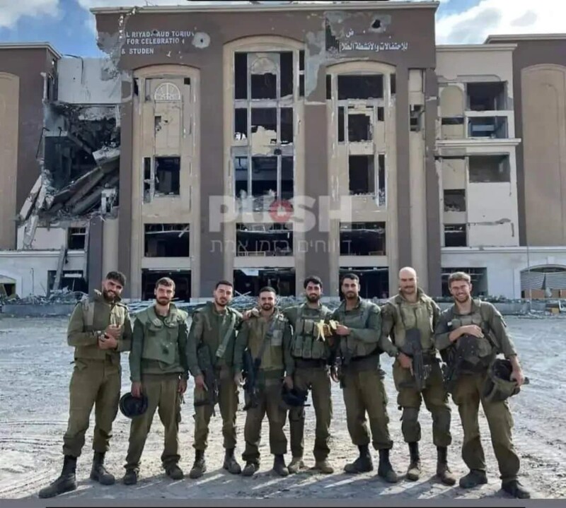 A group of soldiers pose in front of a damaged building