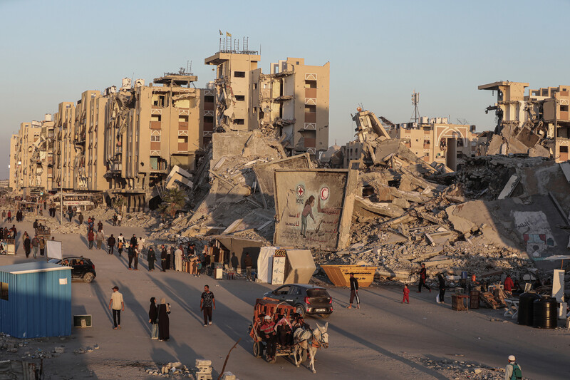 People and donkey carts pass by enormous piles of rubble from bombed buildings