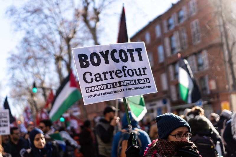 Woman carries sign as others behind her hold Palestinian flags and signs