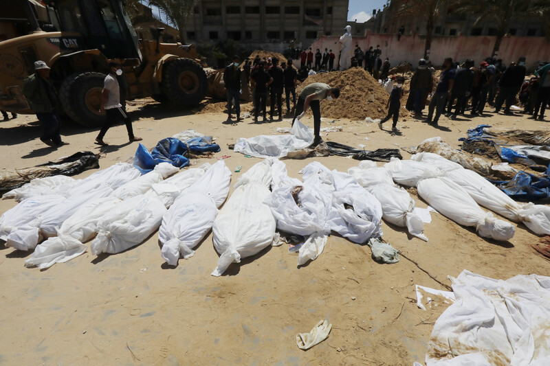 Corpses wrapped in white shrouds are spread across sand ground