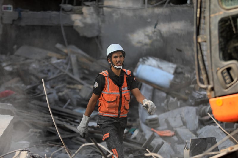 A man in hi viz vest walks through rubble