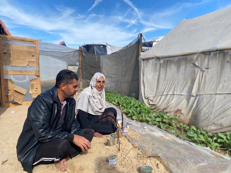 A man and a woman sits next to a strip of cultivated but sandy land