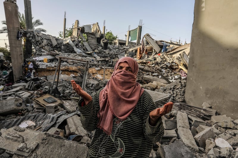 A woman shrugs in front of a destroyed home