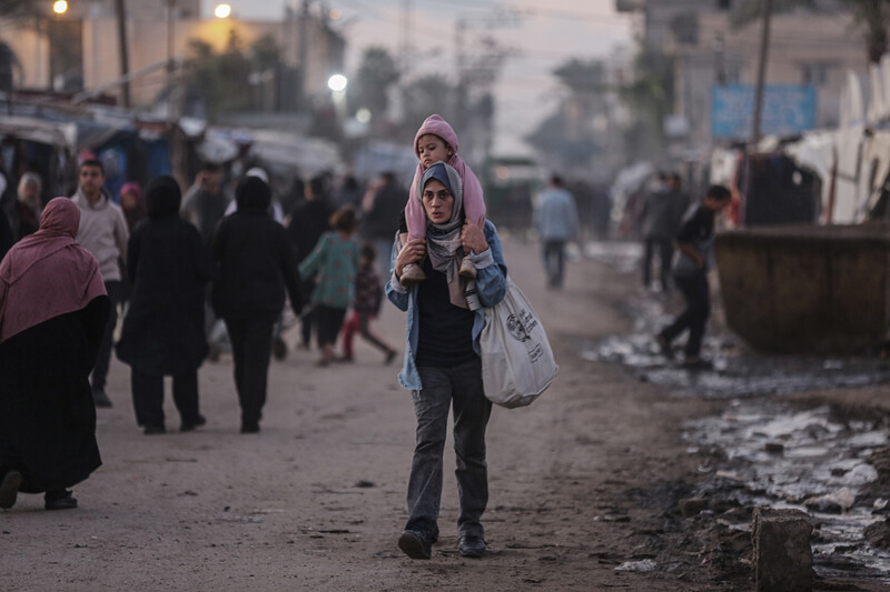 A young woman carries a toddler on her shoulders and holds a bag