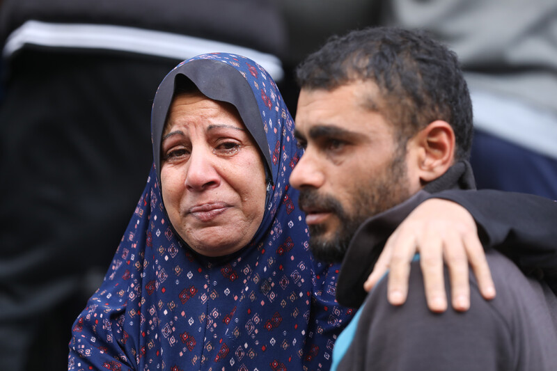 A woman in tears rests an arm around the shoulder of a young man