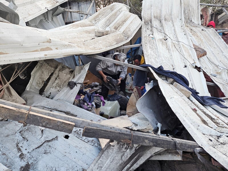 Men sort through personal belongings in a destroyed makeshift shelter