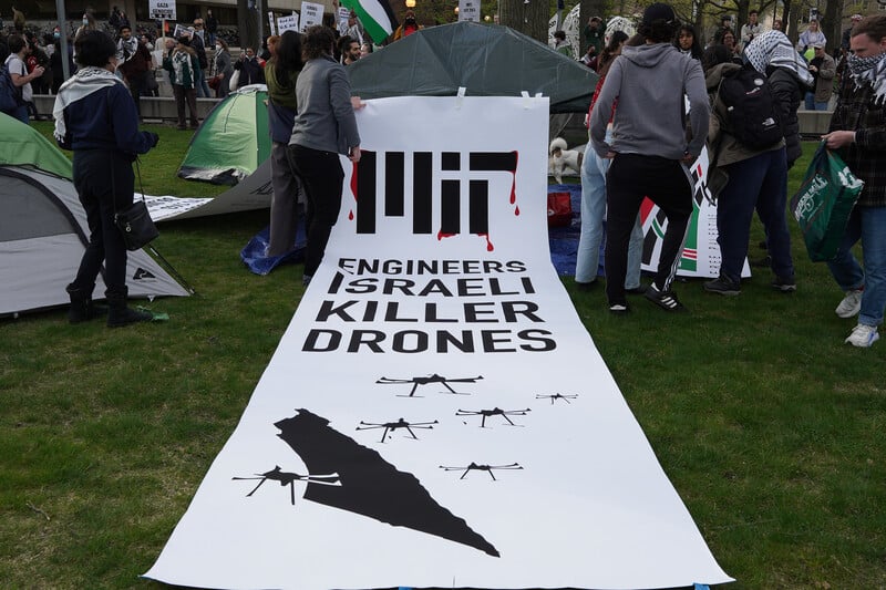 A banner on the ground at a student encampment reads MIT engineers Israeli killer drones