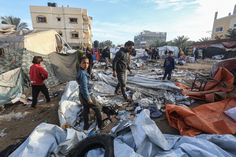 Palestinian children and a man step over the destroyed remains of fabric and plastic tents. 