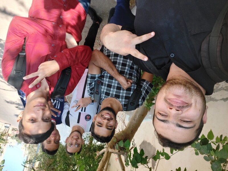 A selfie of five smiling young men making peace sign hand gestures while standing outside