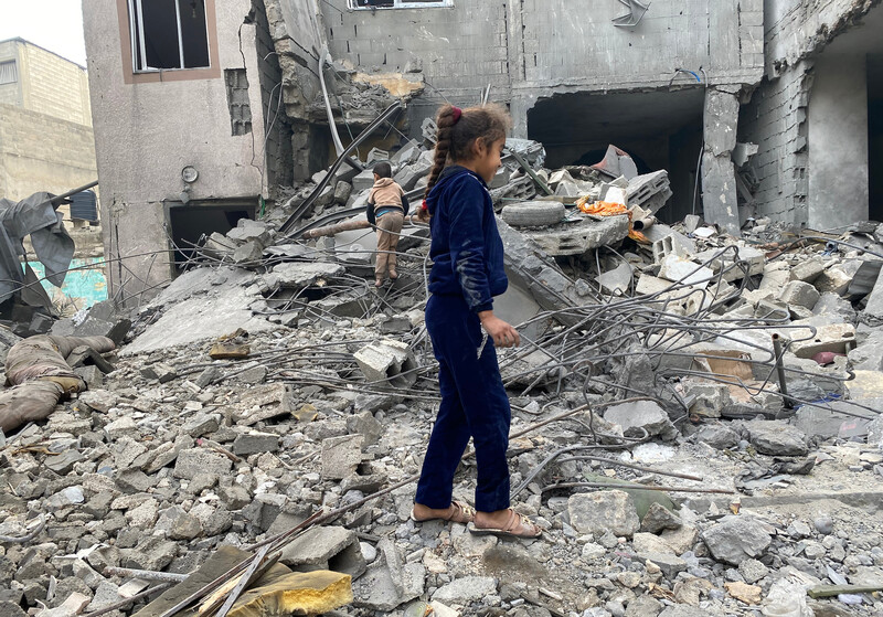 Two young children walk through the rubble of a destroyed house