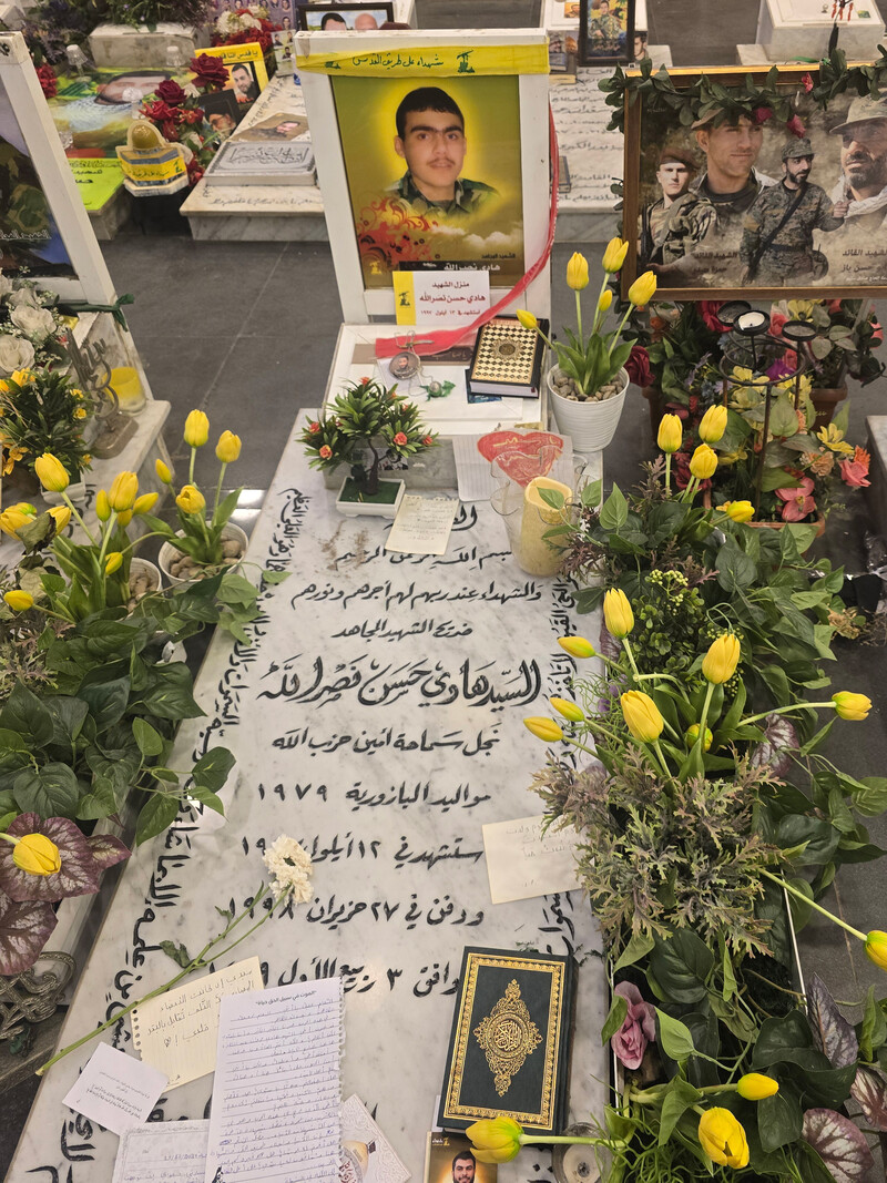 A headstone is surrounded by yellow tulips and a portrait of Hadi Nasrallah