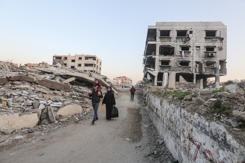 A family walks on a street between destroyed buildings