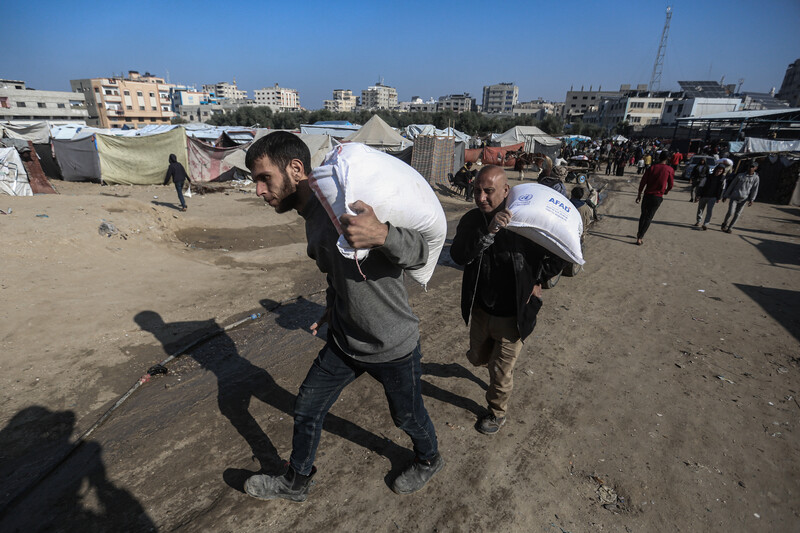 two men carry large bags of flour