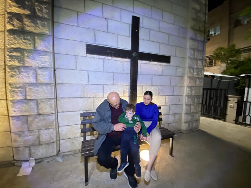 A couple and a toddler sit under a large cross