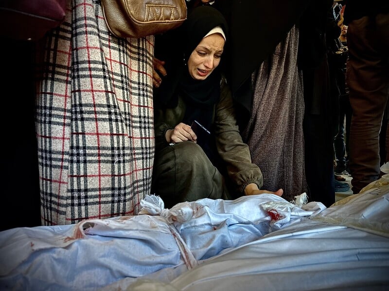 A kneeling woman cries while reaching towards a shrouded body on the ground