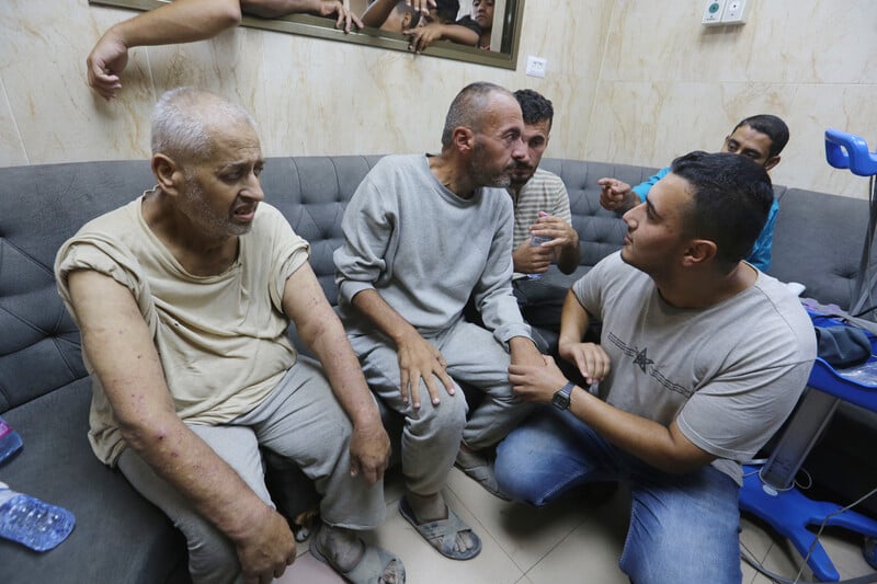 Five Palestinian men seated or squatting with more people in background