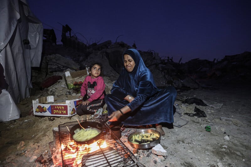 A mother and child prepare food over an open fire