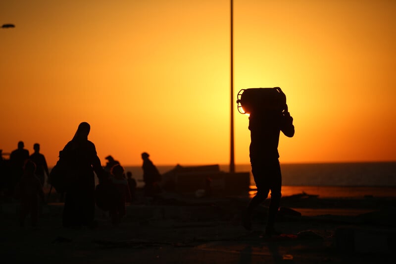 A man in silhouette against a setting sun carries a gas canister