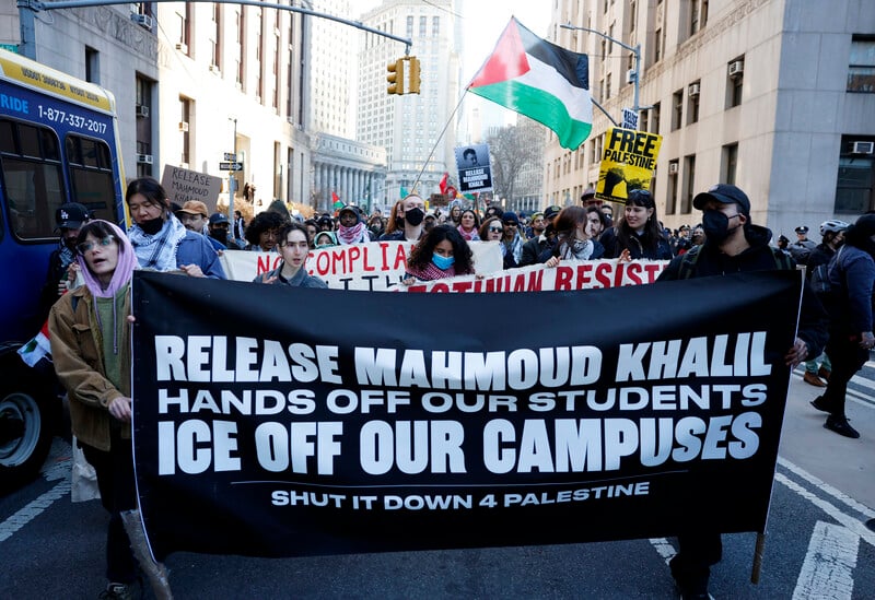 Protesters march with signs and a Palestinian flag