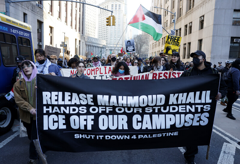 Protesters march with signs and a Palestinian flag