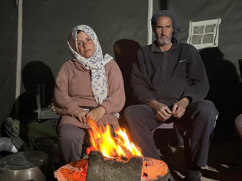 A woman and a man sit behind a fire