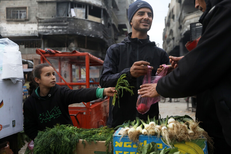 Man and girl selling vegetables hold out produce to a customer