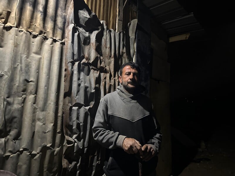 A man stands in front of a makeshift structure