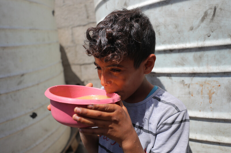 A boy wearing a striped t-shirt lifts a pink bowl to his lips