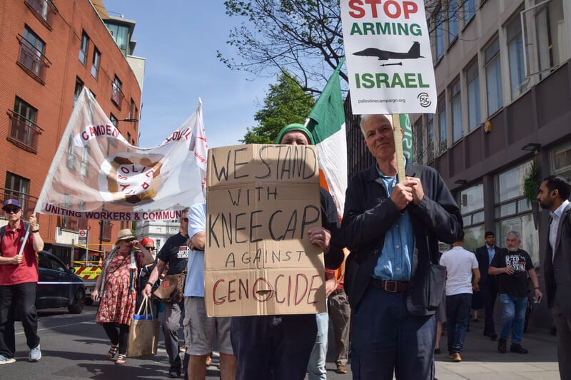 A man holds up a placard voicing support for Kneecap against genocide