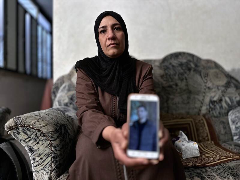A woman holds out a phone with a picture of her son