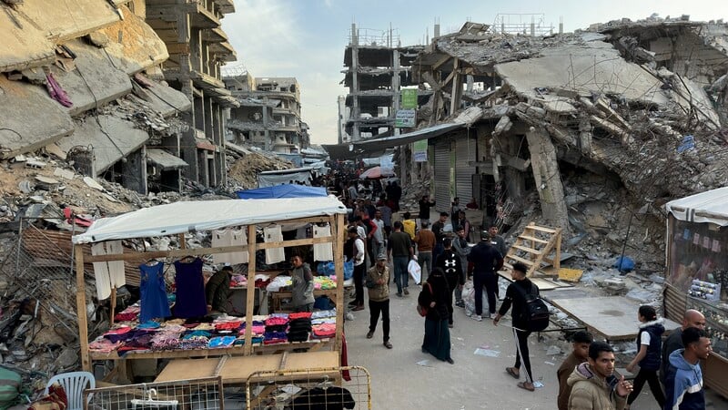 People walk past a small stall amid destroyed buildings 