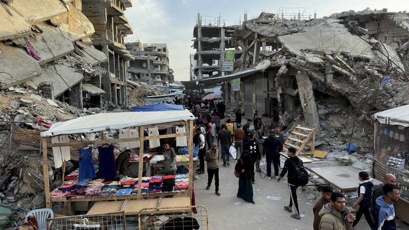 People walk past a small stall amid destroyed buildings