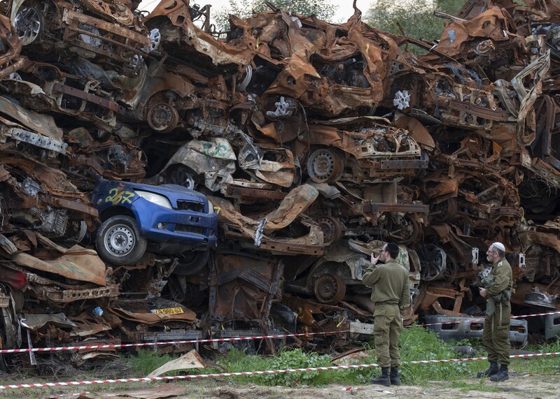 Two soldiers look at a huge stack of car wrecks